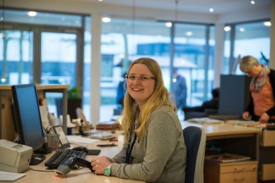Bibliotheksangestellte sitzt am Servicepoint und lächelt in die Kamera
